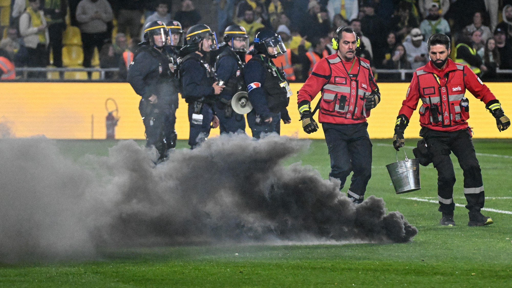 Fire Safety personel run to catch a smoke flare during the French L1 football match between FC Nantes and Toulouse FC at the Stade de la Beaujoire–Louis Fonteneau in Nantes, western France, on May 17, 2026.